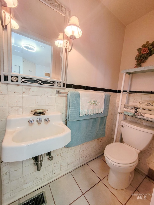 bathroom featuring toilet, tile patterned flooring, tile walls, and a sink