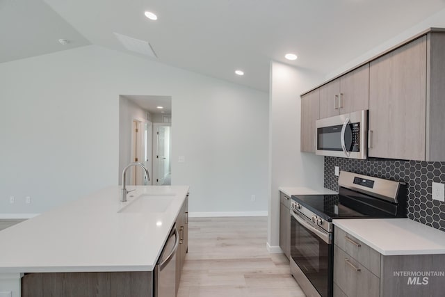 kitchen with vaulted ceiling, appliances with stainless steel finishes, sink, backsplash, and a kitchen island with sink