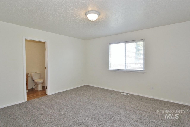 carpeted spare room featuring a textured ceiling and baseboards