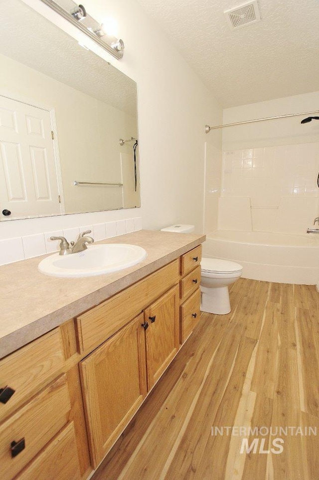 bathroom with toilet, shower / bathtub combination, visible vents, wood finished floors, and vanity