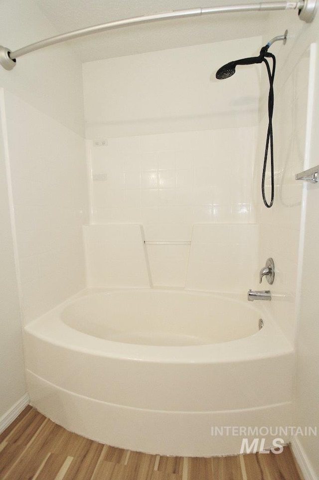 full bath with baseboards, wood finished floors, and washtub / shower combination