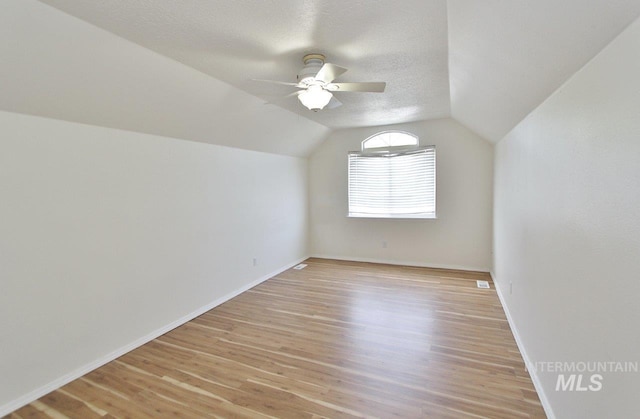 additional living space with a textured ceiling, light wood-type flooring, vaulted ceiling, baseboards, and a ceiling fan