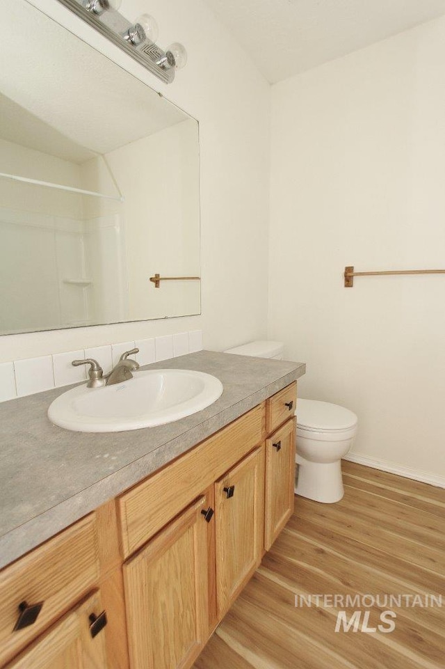 full bath with toilet, vanity, wood finished floors, and baseboards