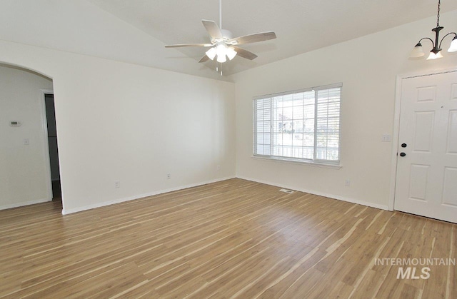 foyer featuring lofted ceiling, arched walkways, baseboards, light wood-style flooring, and ceiling fan with notable chandelier
