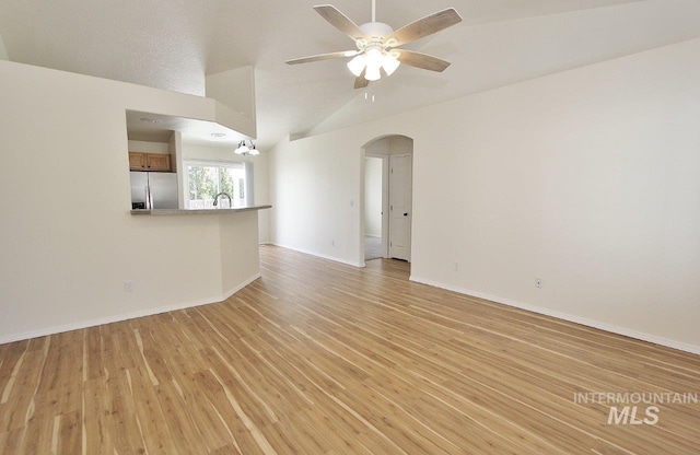 unfurnished living room featuring arched walkways, vaulted ceiling, baseboards, light wood-style floors, and ceiling fan