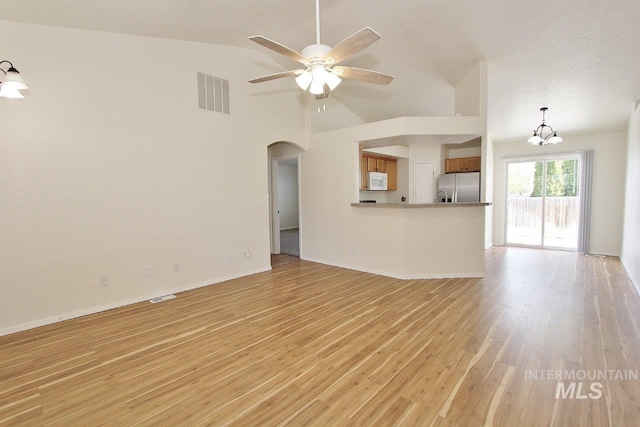 unfurnished living room with light wood-style flooring, arched walkways, vaulted ceiling, visible vents, and ceiling fan with notable chandelier