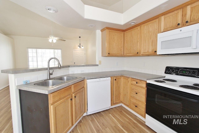 kitchen featuring a peninsula, a sink, white appliances, and light wood-type flooring