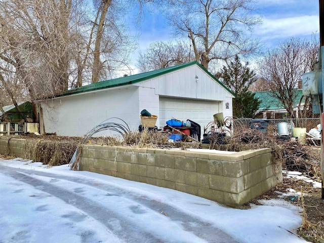 view of snowy exterior with concrete block siding, fence, and an outbuilding