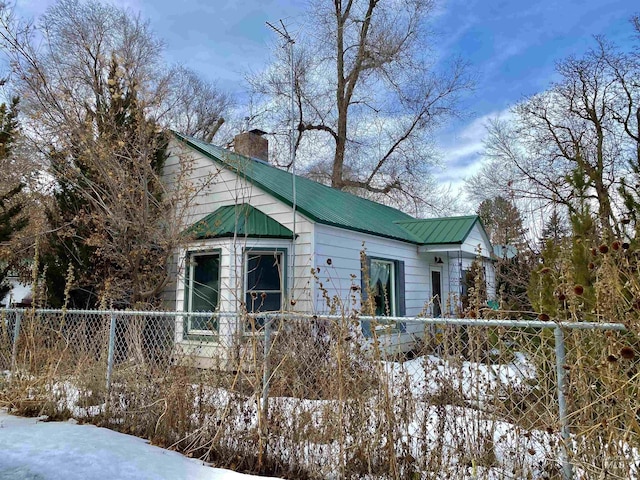 snow covered property with a fenced front yard, metal roof, and a chimney