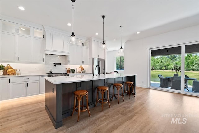 124 S Eagles Roost Way, Eagle, ID 83616 - kitchen featuring light wood-style flooring, an island with sink, white cabinetry, light countertops, and backsplash