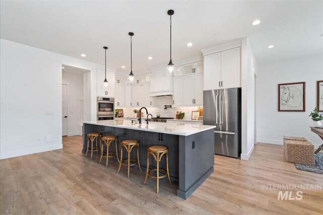 124 S Eagles Roost Way, Eagle, ID 83616 - kitchen with appliances with stainless steel finishes, light wood finished floors, white cabinets, a kitchen bar, and recessed lighting