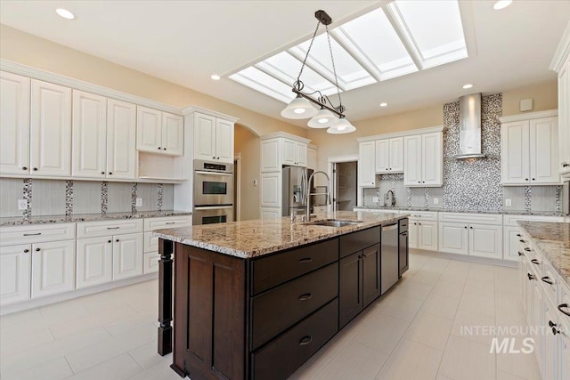 kitchen with wall chimney exhaust hood, white cabinets, backsplash, a skylight, and appliances with stainless steel finishes