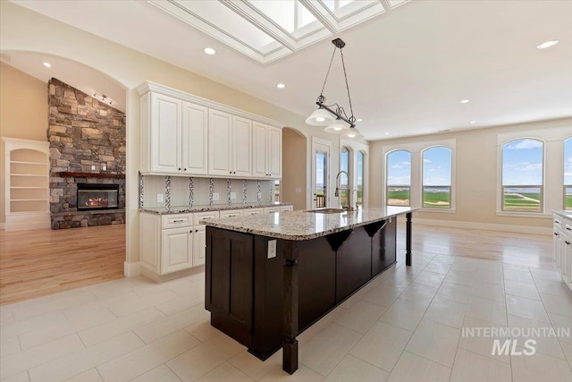 kitchen featuring an island with sink, white cabinetry, light stone countertops, and a sink