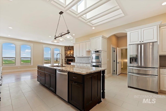 kitchen with a sink, a skylight, decorative backsplash, light tile patterned floors, and appliances with stainless steel finishes