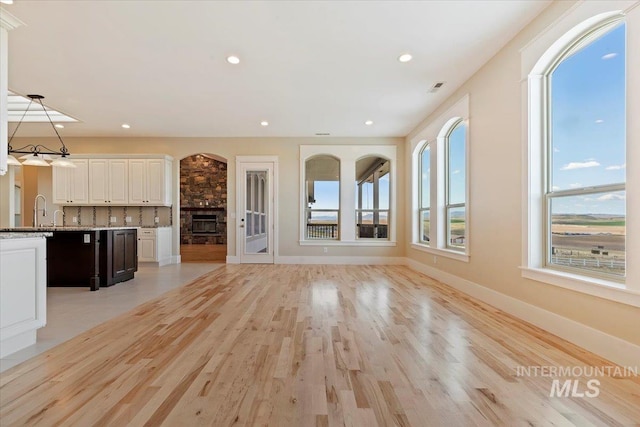 unfurnished living room with light wood finished floors, a sink, baseboards, visible vents, and a fireplace