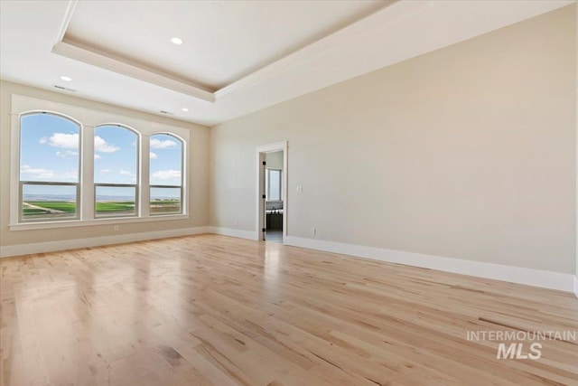 empty room featuring baseboards, recessed lighting, light wood-style floors, and a tray ceiling