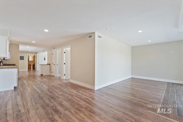 unfurnished living room with light wood-type flooring, a sink, visible vents, and recessed lighting