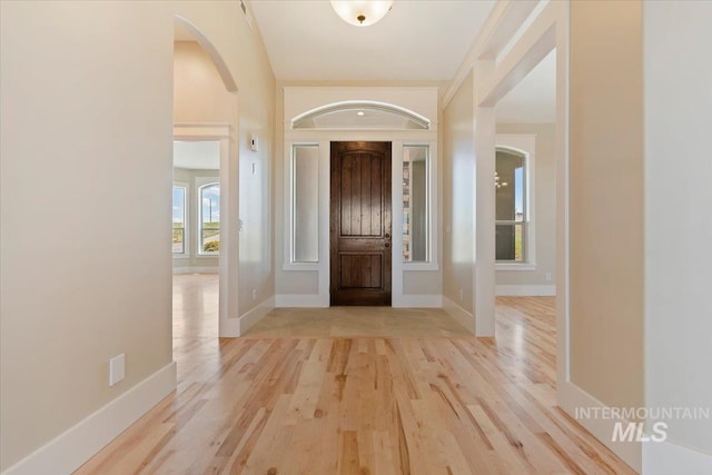 entryway with arched walkways, light wood finished floors, and baseboards