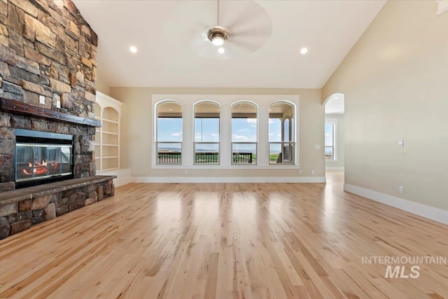 unfurnished living room with baseboards, arched walkways, wood finished floors, and a fireplace