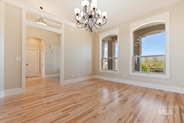 spare room featuring arched walkways, wood finished floors, baseboards, and an inviting chandelier