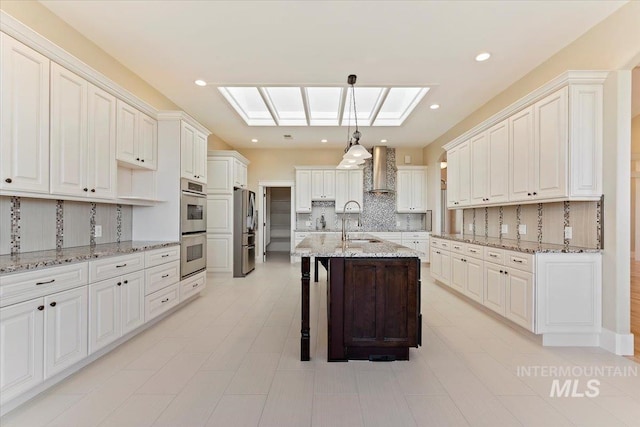 kitchen with stainless steel appliances, a kitchen bar, decorative backsplash, wall chimney range hood, and an island with sink