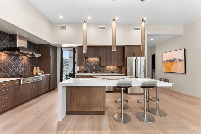 119 S 10th Unit 605, Boise, ID 83702 - kitchen featuring wall chimney range hood, appliances with stainless steel finishes, light wood-style flooring, a center island, and light countertops