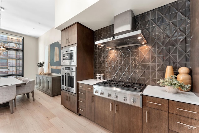 119 S 10th Unit 605, Boise, ID 83702 - kitchen with appliances with stainless steel finishes, wall chimney exhaust hood, tasteful backsplash, light wood-type flooring, and light countertops