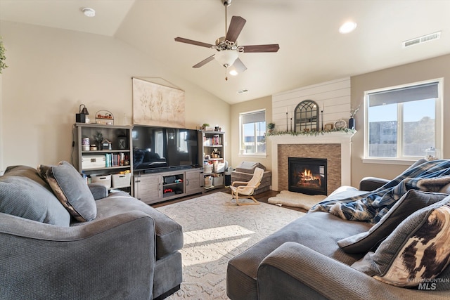 living area featuring lofted ceiling, a lit fireplace, visible vents, and a wealth of natural light