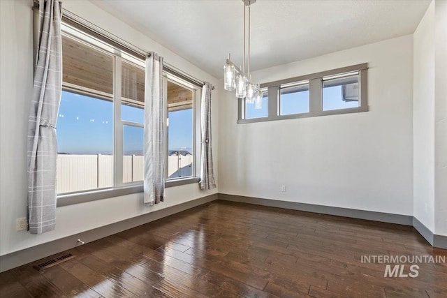 empty room with a wealth of natural light and dark hardwood / wood-style flooring