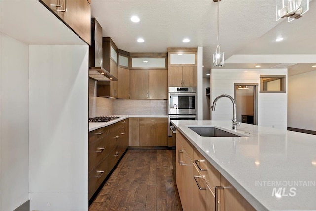 kitchen with hanging light fixtures, appliances with stainless steel finishes, sink, dark wood-type flooring, and wall chimney range hood