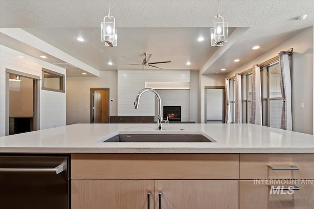 kitchen featuring sink, stainless steel dishwasher, light brown cabinetry, and hanging light fixtures