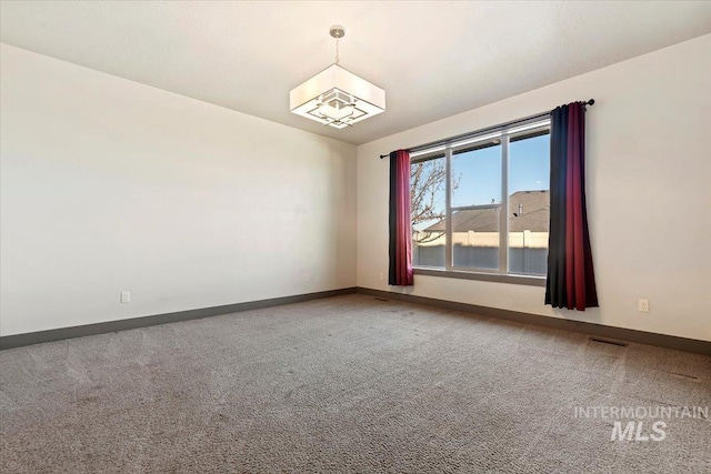 carpeted spare room featuring a chandelier