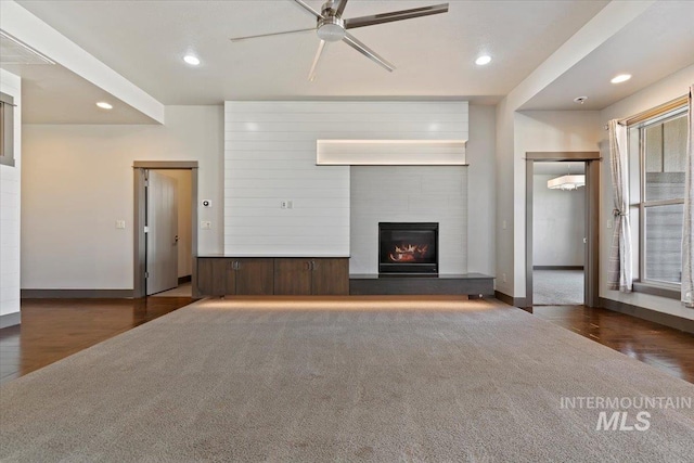 unfurnished living room with ceiling fan, dark wood-type flooring, and a tiled fireplace