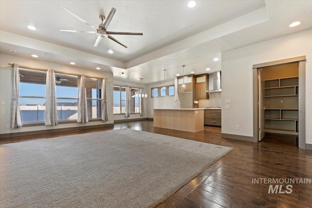 unfurnished living room featuring ceiling fan, a water view, a tray ceiling, a textured ceiling, and dark hardwood / wood-style floors