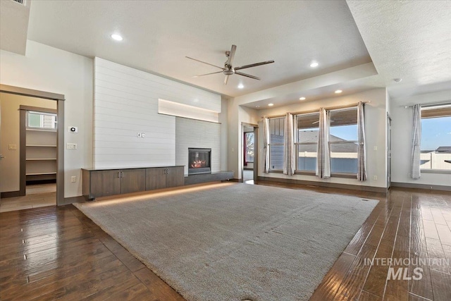 unfurnished living room with ceiling fan, a large fireplace, dark hardwood / wood-style floors, and a textured ceiling