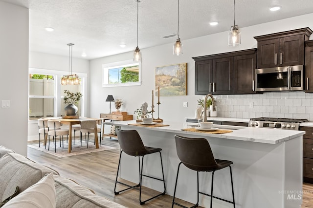 1753 E Grayson, Meridian, ID 83642 - kitchen with stainless steel microwave, tasteful backsplash, a breakfast bar, dark brown cabinets, and light wood finished floors