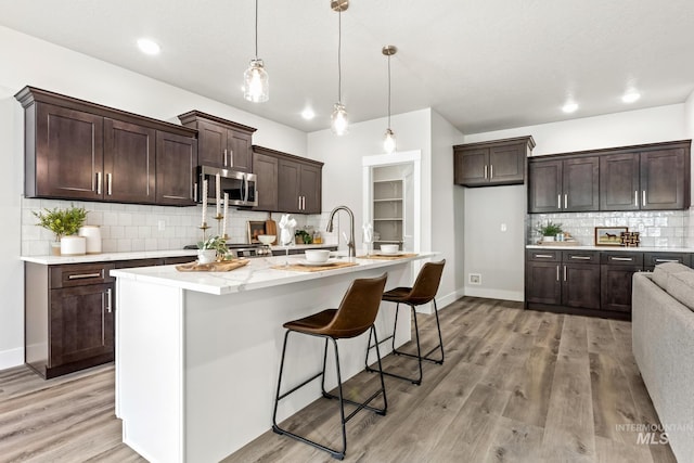 1753 E Grayson, Meridian, ID 83642 - kitchen with stainless steel microwave, backsplash, light wood-style floors, dark brown cabinetry, and baseboards