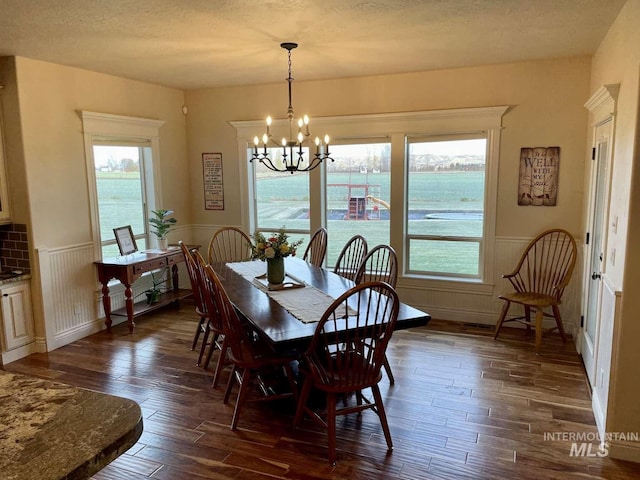 dining room featuring a chandelier, a wainscoted wall, a textured ceiling, and dark wood-type flooring