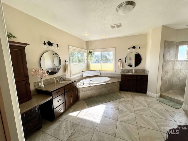 bathroom with a walk in shower, a garden tub, two vanities, a textured ceiling, and a sink