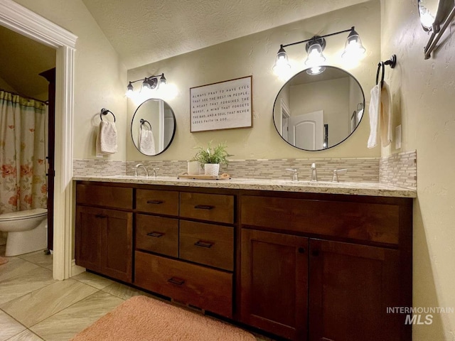 bathroom featuring toilet, a sink, tasteful backsplash, a textured ceiling, and double vanity