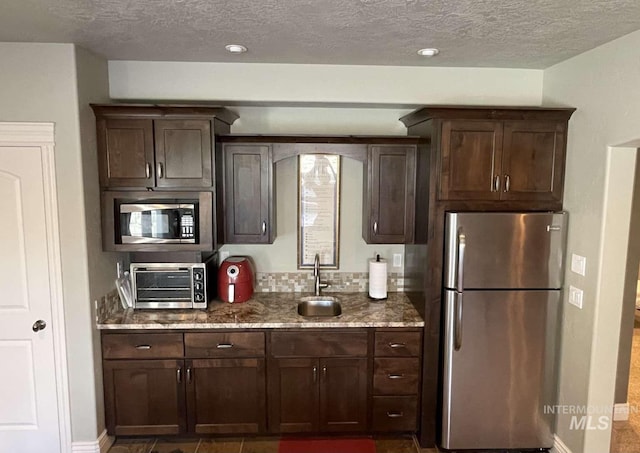 kitchen featuring dark brown cabinets, light stone countertops, stainless steel appliances, and a sink