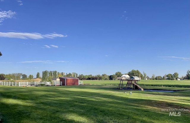 view of yard with a rural view, an outbuilding, fence, and playground community