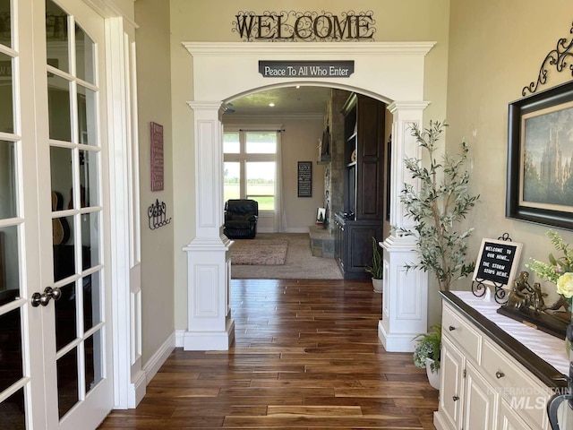 hall featuring dark wood-type flooring, ornamental molding, french doors, arched walkways, and ornate columns