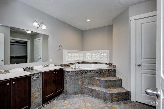 bathroom with a sink, a walk in closet, a garden tub, and two vanities