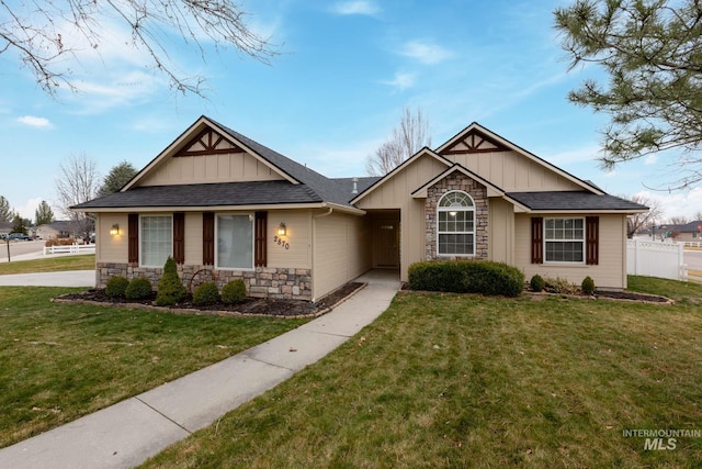 view of front of house featuring board and batten siding, a front yard, fence, and stone siding