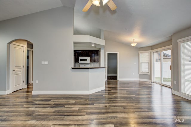 unfurnished living room with arched walkways, dark wood-style flooring, plenty of natural light, and vaulted ceiling