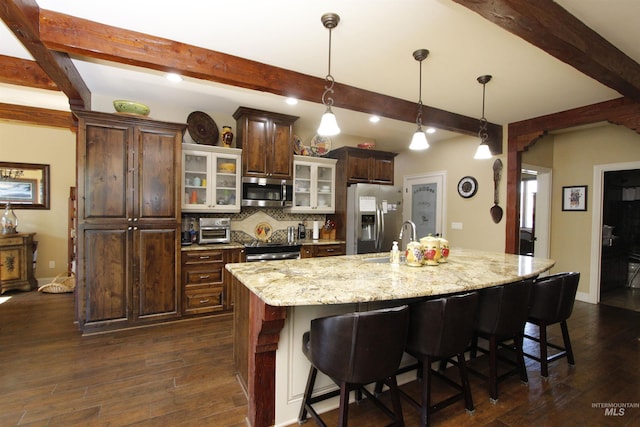 kitchen with a kitchen bar, a sink, dark wood-style floors, stainless steel appliances, and an island with sink