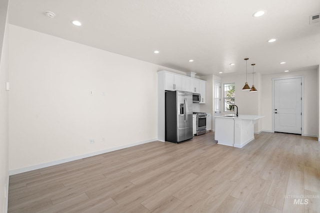 kitchen with a center island with sink, appliances with stainless steel finishes, decorative light fixtures, light countertops, and white cabinetry