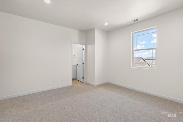 spare room featuring light colored carpet, visible vents, a textured ceiling, and baseboards