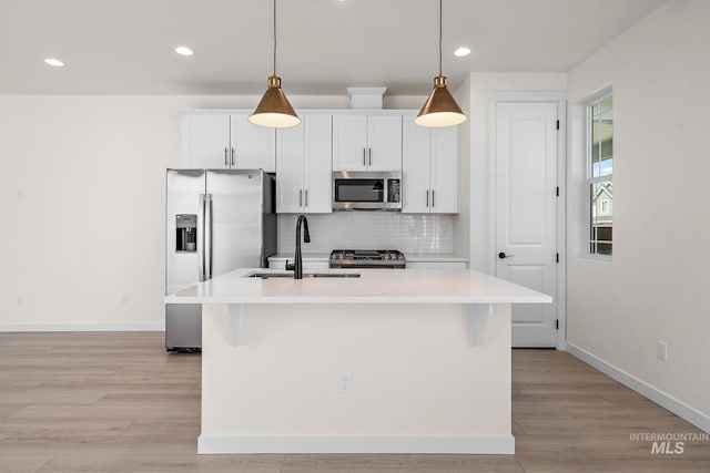 kitchen with an island with sink, appliances with stainless steel finishes, light countertops, and decorative light fixtures